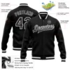 Black custom varsity jacket with white striped cuffs, personalized team name on the front, and custom name with number on the back.